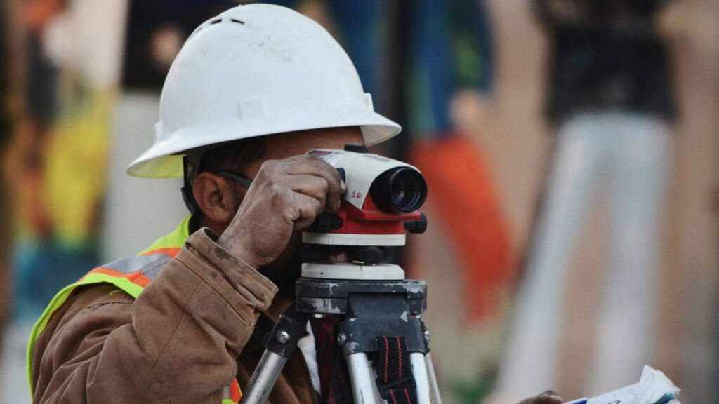 A construction worker in the process of using a camera with a tripod