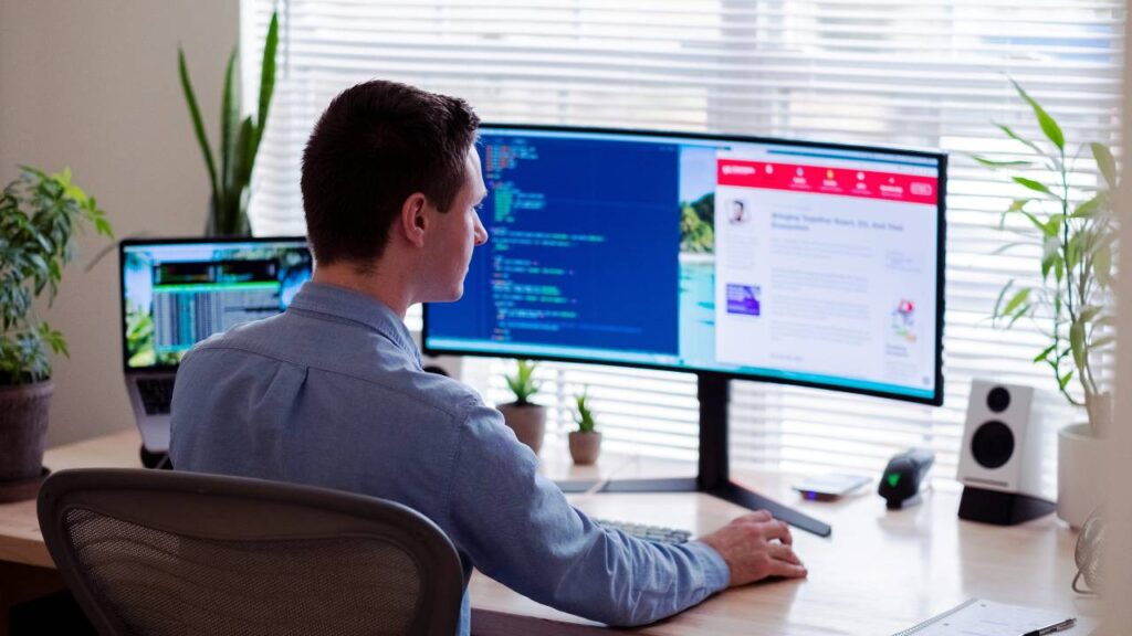 A remote worker sitting in front of a large widescreen monitor