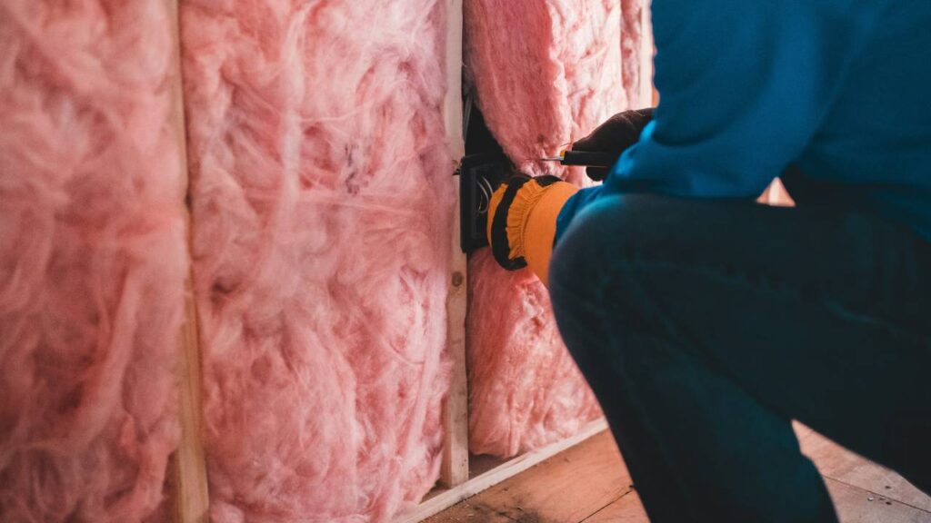 A handyman in the process of installing pink insulation