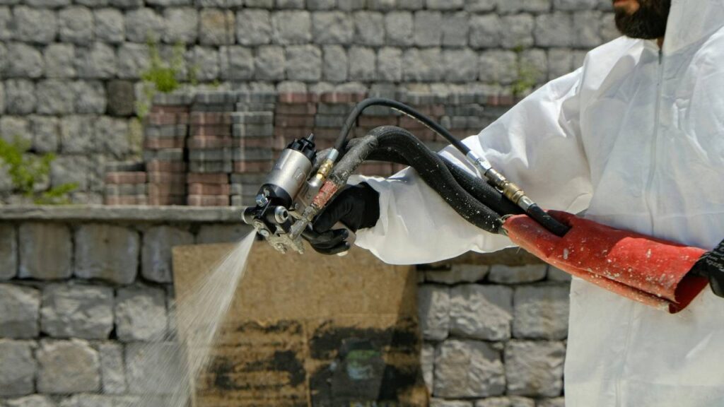 A man in white hazard suit spraying insulation