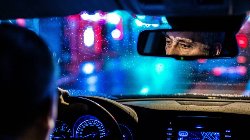 Chauffeur's face seen in the car's interior rearview mirror