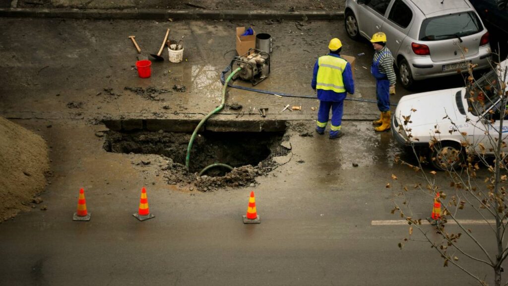 Several men draining water from a hole in the road 