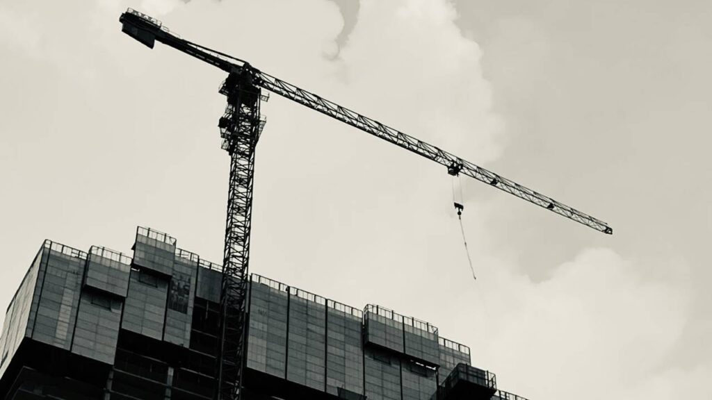 A black and white photo of a construction crane next to a building